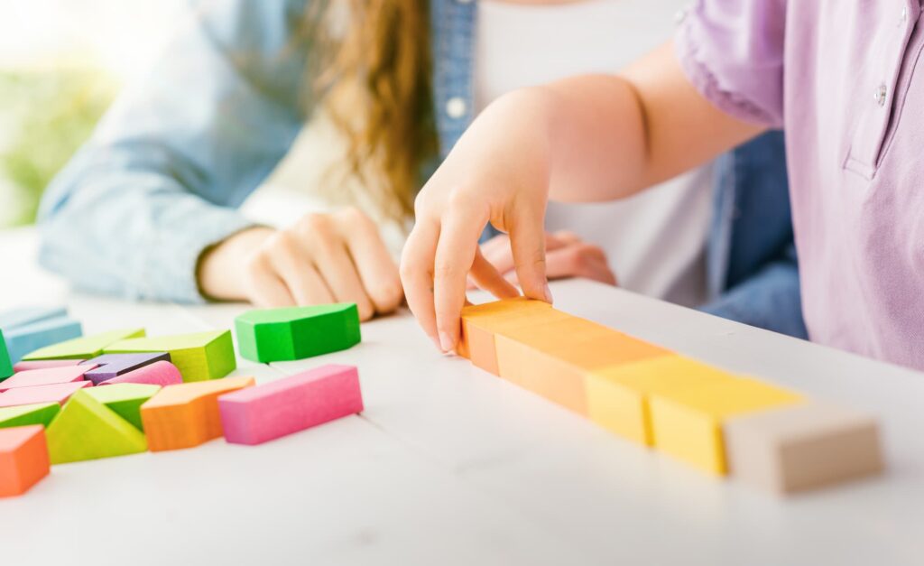 Un adulte joue avec un jeune enfant à un jeu de cubes en bois.